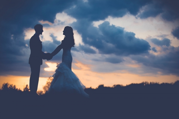 silhouette of man and woman standing under cloudy skies during orange sunset